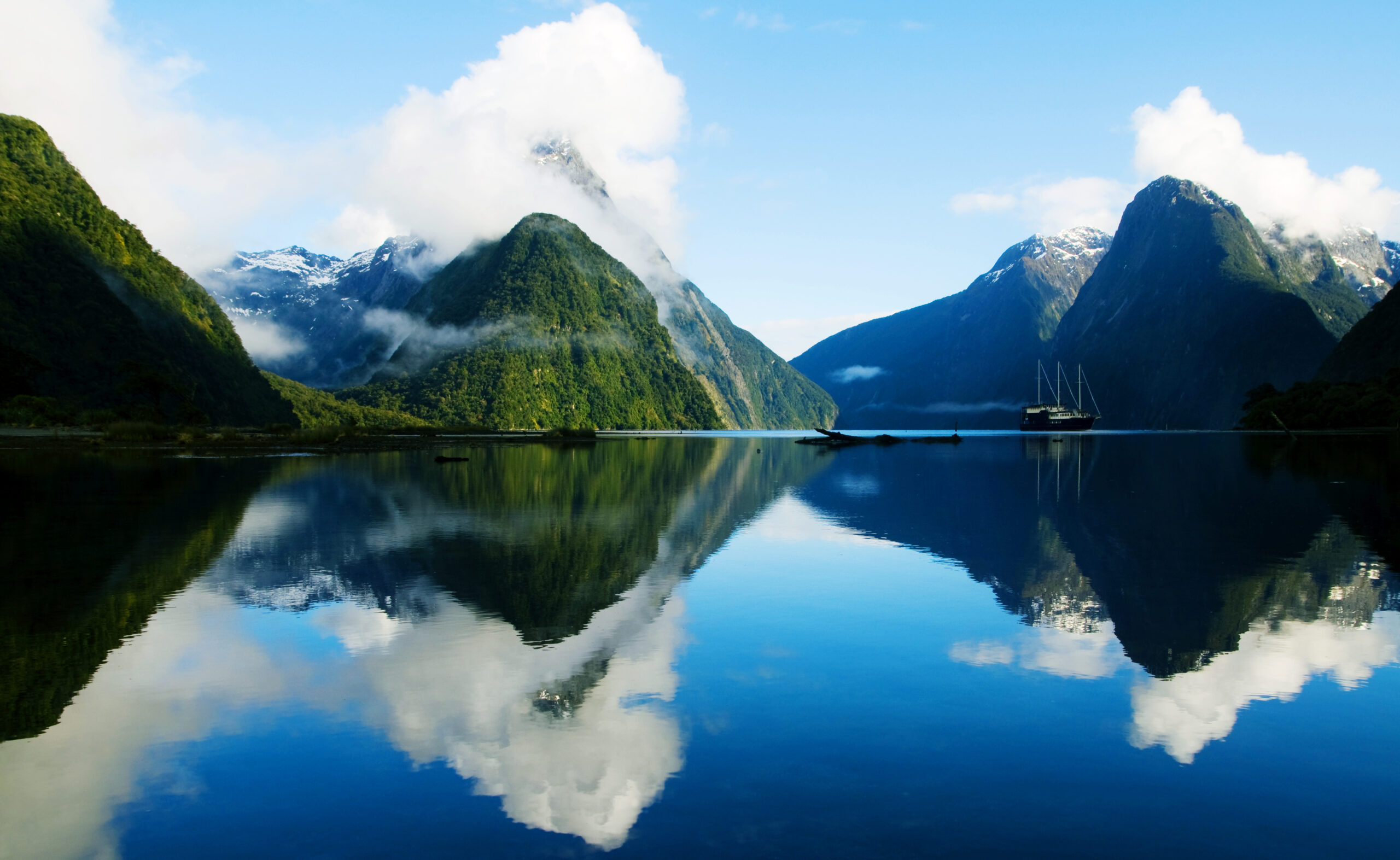 Sydney Harbour at Twilight with Opera House A three-masted sailing vessel anchors in the pristine waters of Milford Sound, surrounded by dramatic snow-capped peaks and lush green-forested mountains.