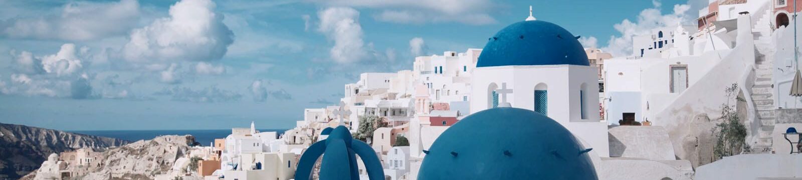 A picturesque view of Oia, Santorini featuring iconic white-washed buildings and distinctive blue-domed churches against a backdrop of blue sky and sea.