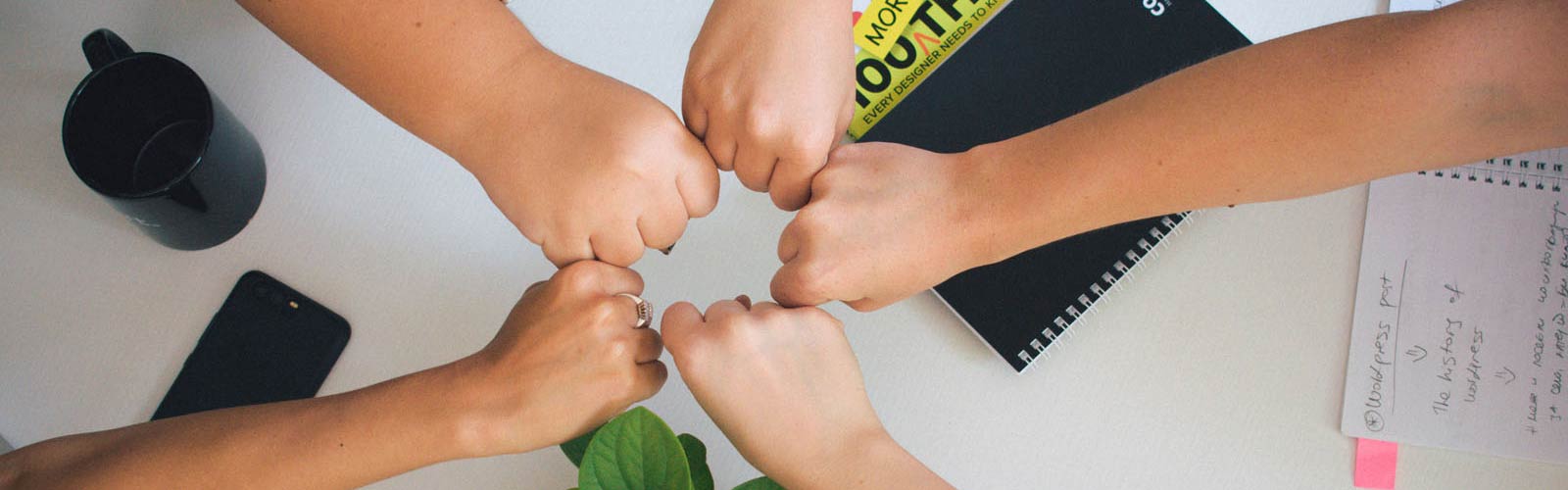 A view from above showing multiple hands in a fist bump, symbolizing teamwork and collective agreement in a workspace setting with office items nearby.