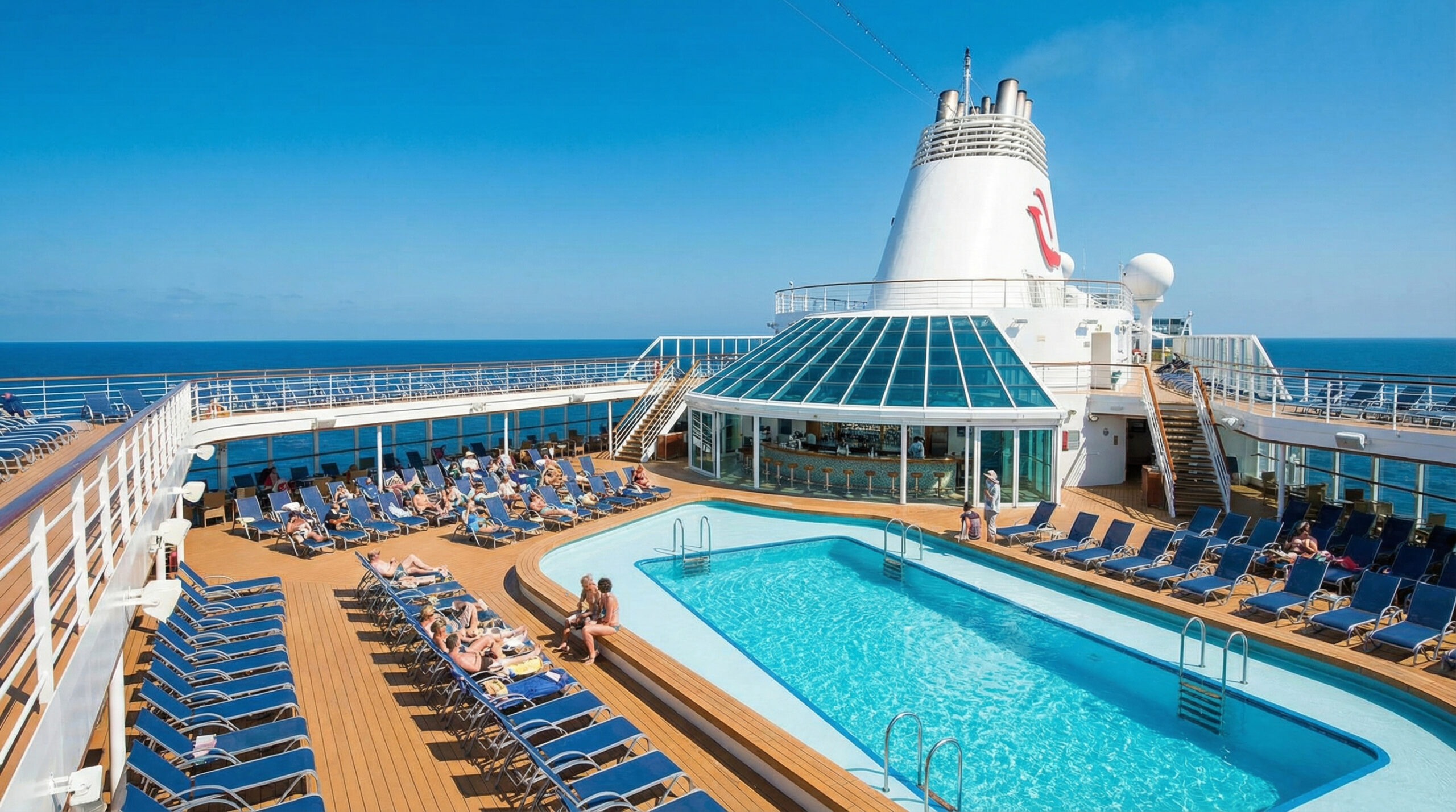 Cruise ship pool deck with swimming pool, blue lounge chairs, and funnel in bright sunshine at sea