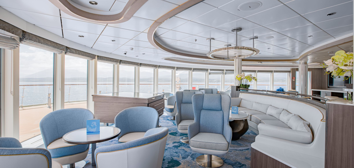 Modern cruise ship observation lounge with blue seating, floor-to-ceiling windows overlooking ocean