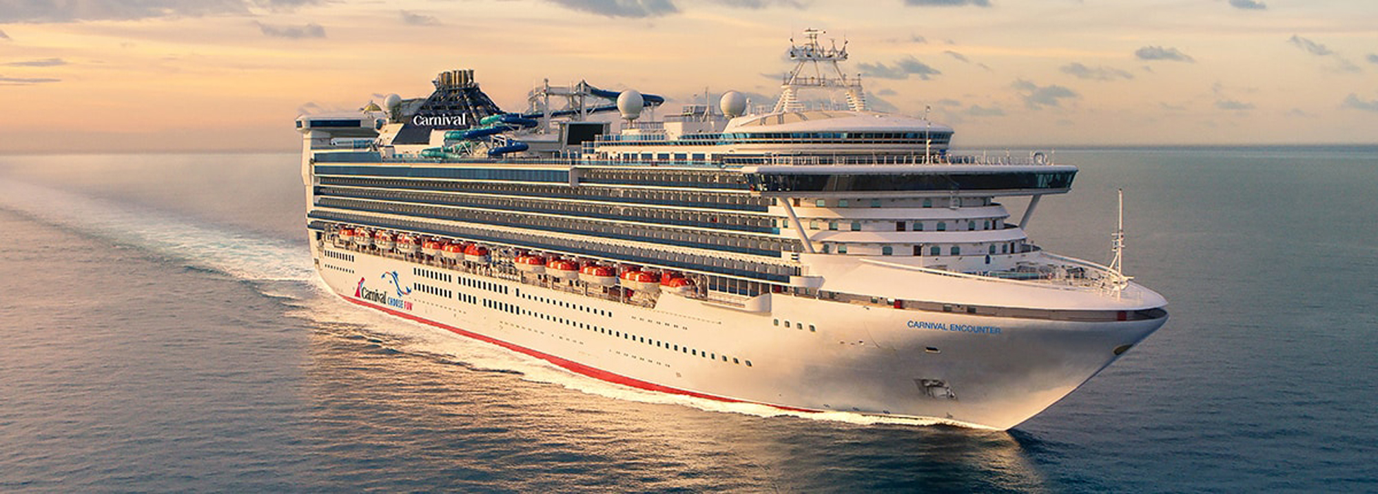 A large white Carnival cruise ship sailing across calm waters during sunset, creating a serene