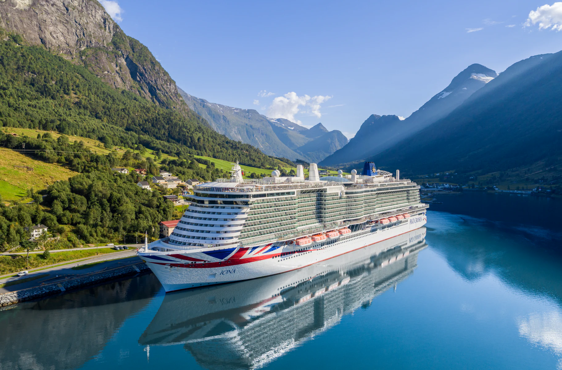 A large modern cruise ship is moored in a pristine Norwegian fjord surrounded by dramatic steep