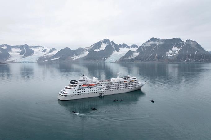 A white cruise ship navigating through calm, reflective waters surrounded by snow-capped
