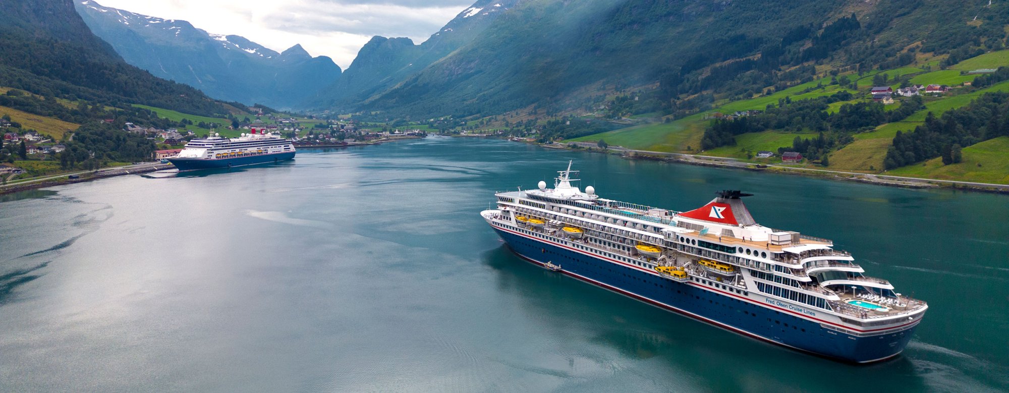 Two large cruise ships anchored in a pristine turquoise fjord surrounded by dramatic snow-capped