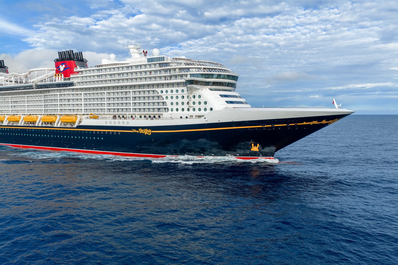 A large white and navy blue Disney Cruise Line ship sailing on open blue waters under a cloudy sky