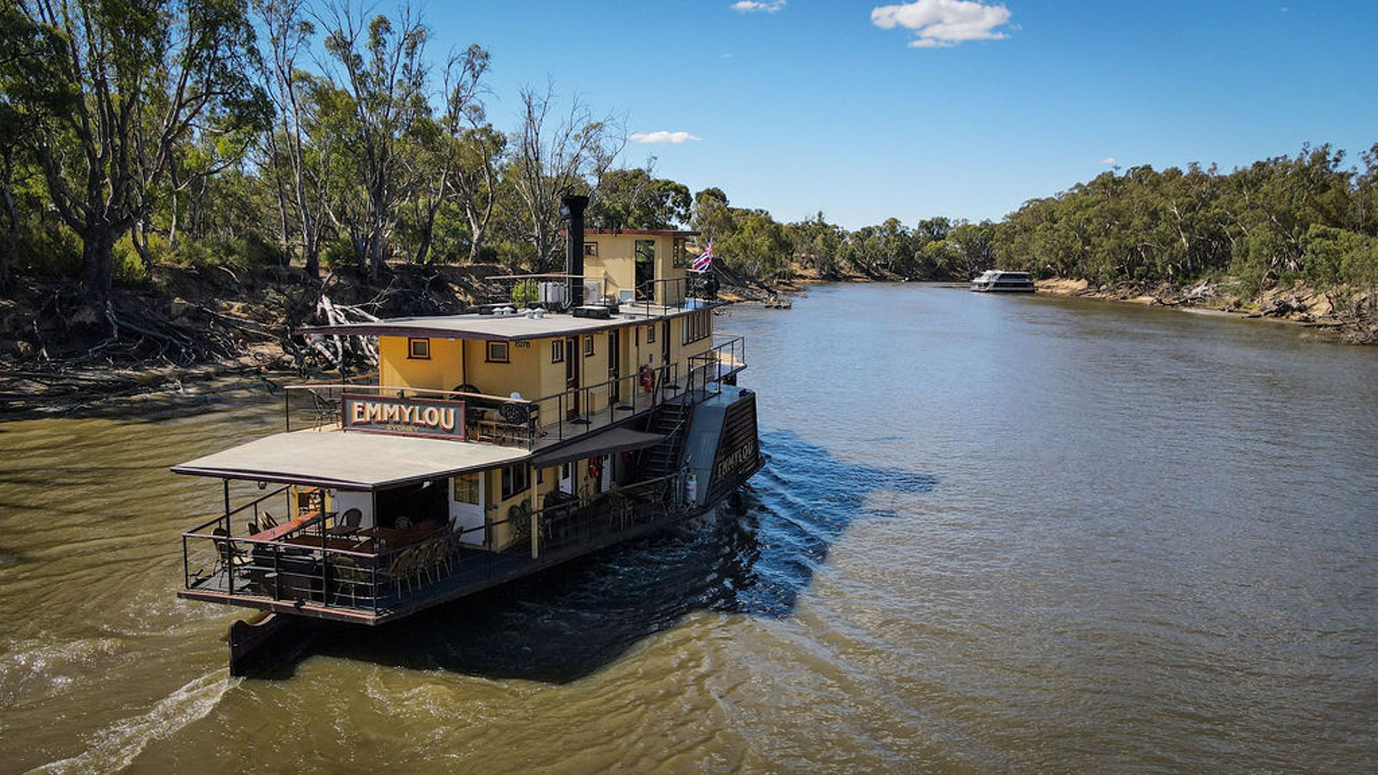 A charming yellow and cream paddlewheel riverboat named Emmylou is moored along the Murray River