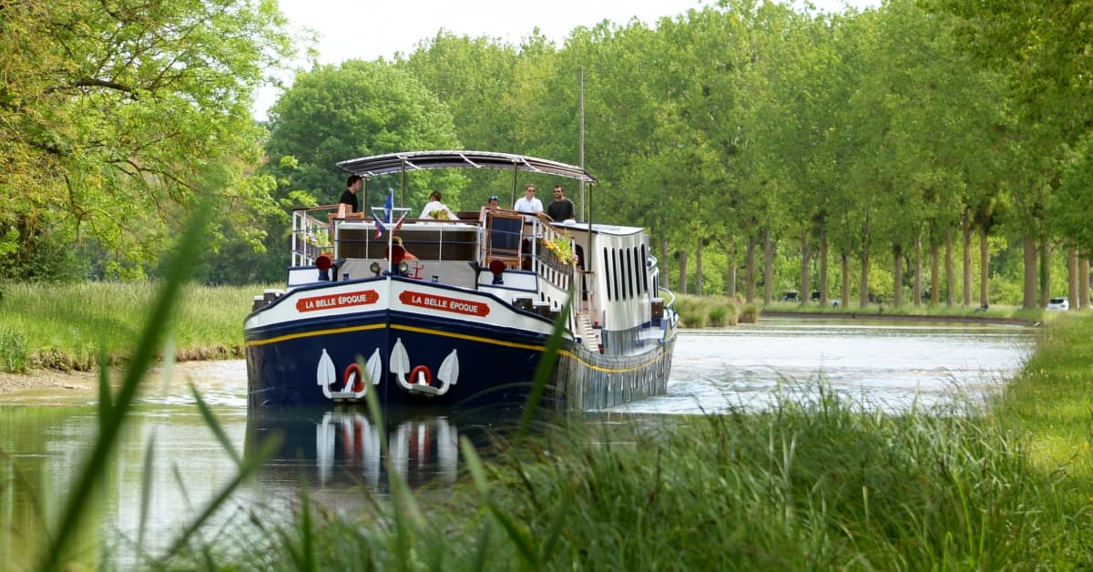 A charming river cruise boat named 'La Belle Époque' navigates through a scenic waterway lined