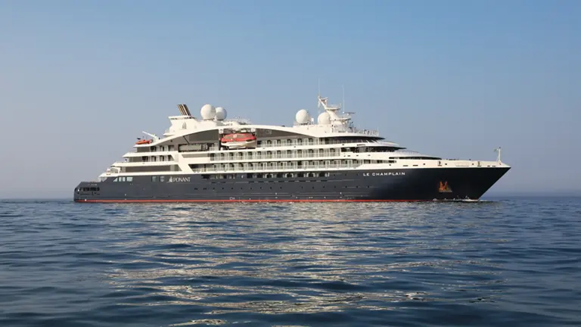 A sleek white and dark gray luxury expedition cruise ship sailing on calm blue waters. The vessel