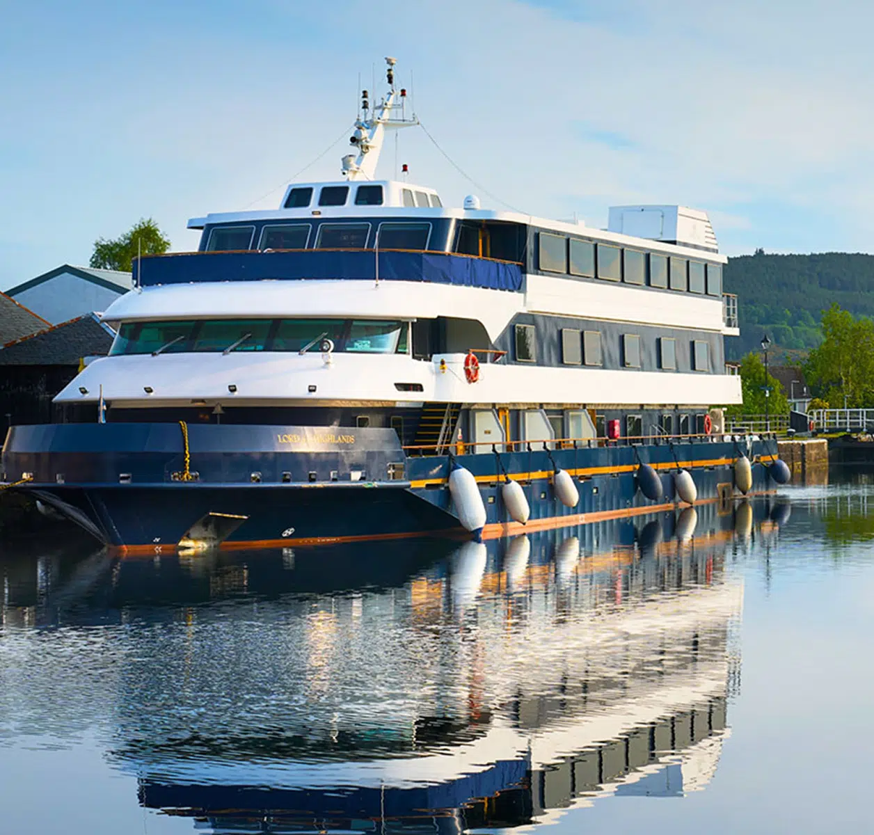 A sophisticated three-deck expedition cruise vessel moored at a riverside dock, featuring