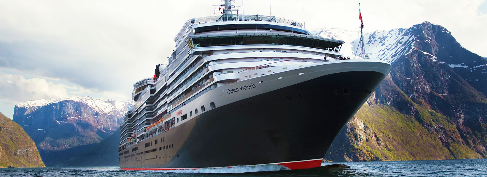 A large Cunard cruise ship, the Queen Victoria, sailing through a scenic fjord with snow-capped