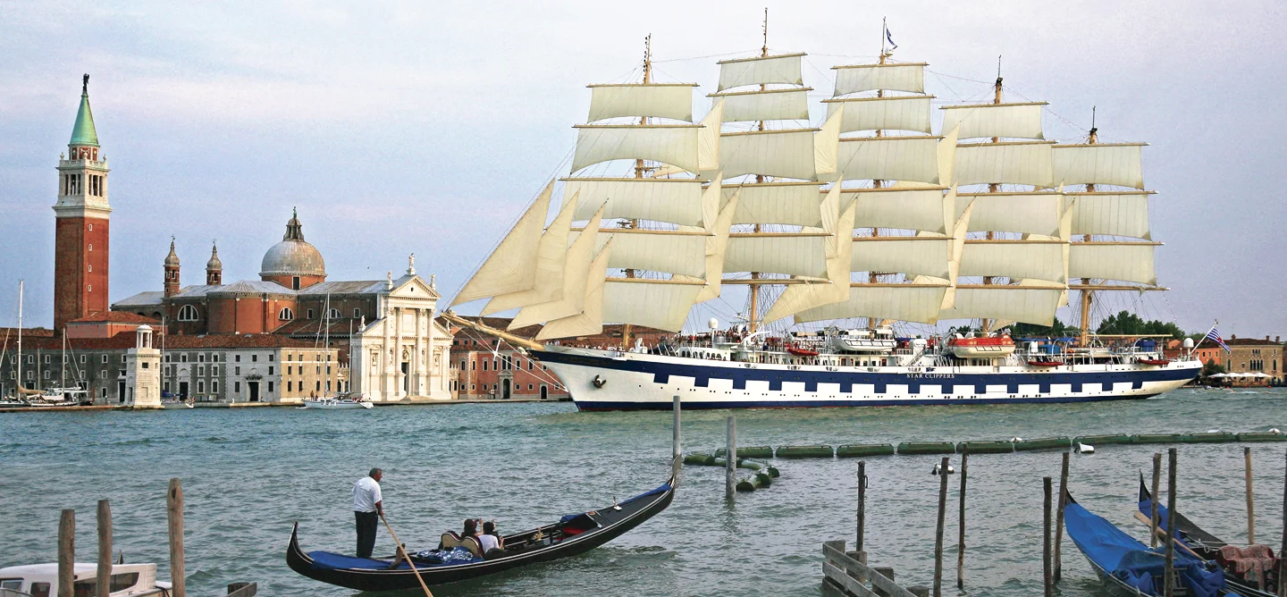 A magnificent multi-masted sailing vessel with full white sails anchored in the Venice lagoon