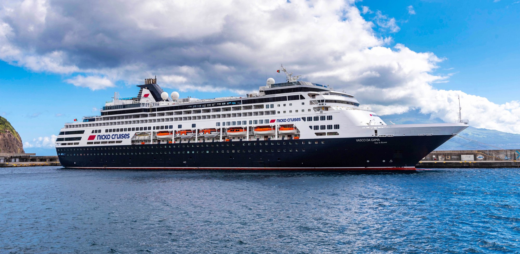 The Vasco da Gama, a large Nicko Cruises ocean liner, is moored in a picturesque harbor