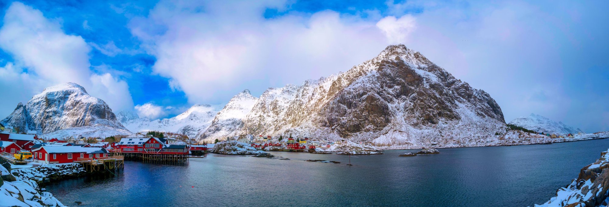 Dramatic Norwegian fjord scenery with towering cliff faces, cascading waterfalls, and mirror-still waters reflecting snow-capped mountains under a bright northern sky.