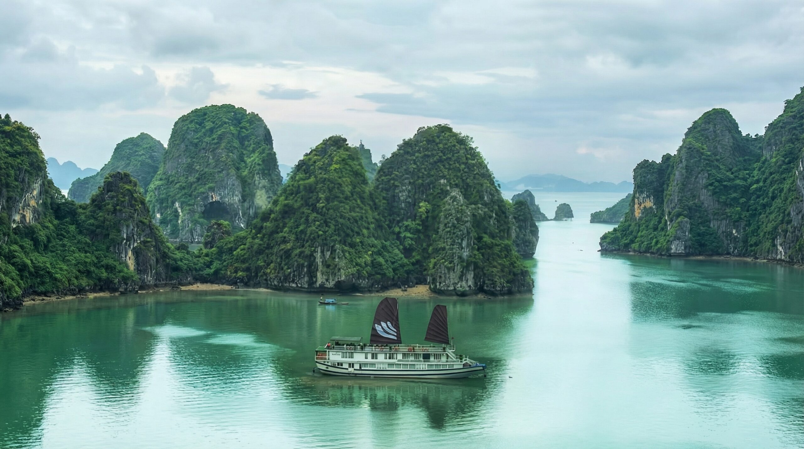 Bhaya Classic junk with dark sails in Halong Bay surrounded by limestone karsts