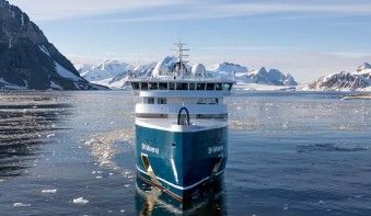 A modern expedition cruise ship navigates through icy Arctic waters with snow-capped mountains
