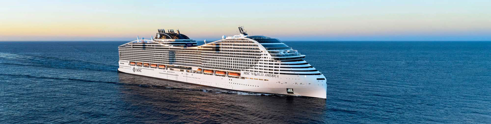 A massive modern cruise ship, the MSC World America, sails through calm blue waters during golden