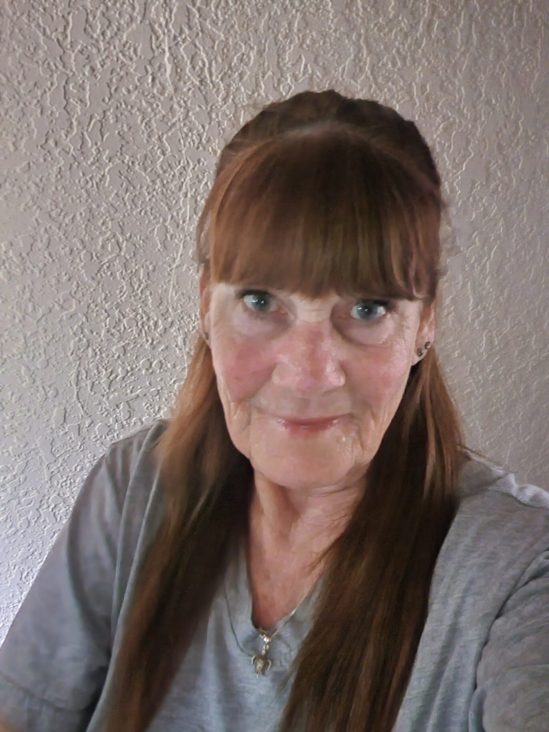 Woman with brown hair and bangs wearing glasses and gray top against textured white wall