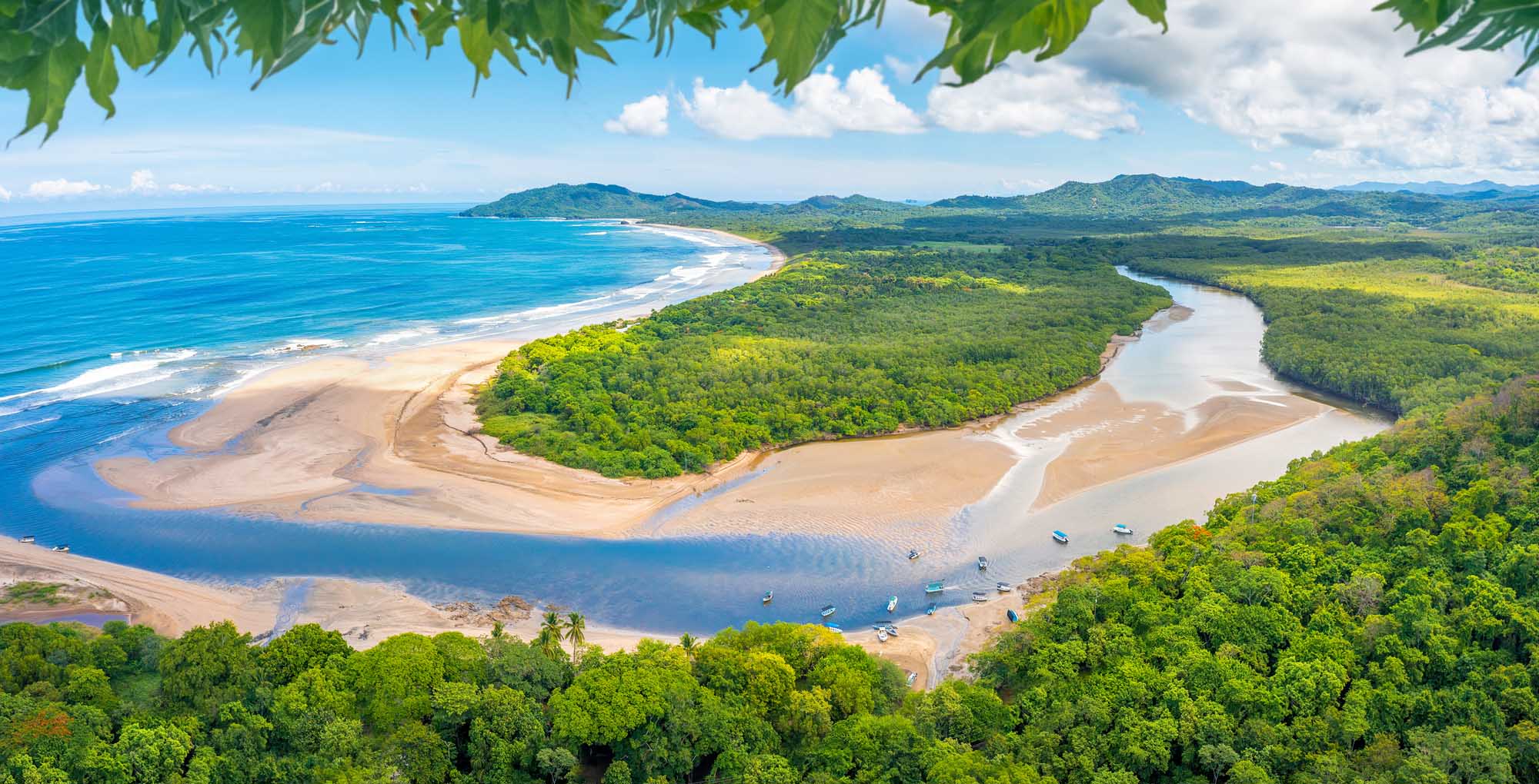 An aerial view of Tamarindo Beach and its river estuary in Guanacaste, Costa Rica, showcasing pristine sandy beaches meeting turquoise waters, lush tropical rainforest vegetation, and a winding river delta.