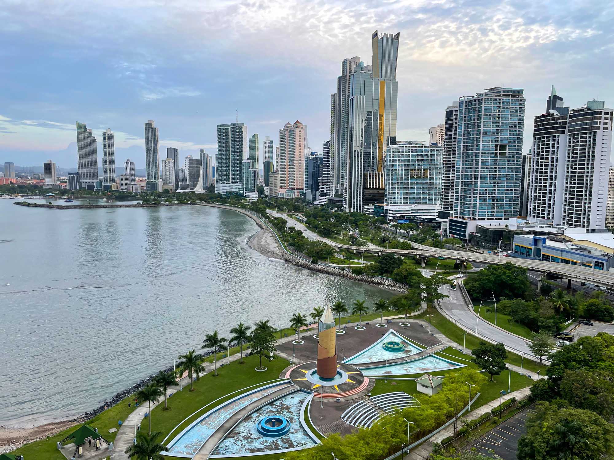 A panoramic view of the Gold Coast's modern high-rise skyline stretching along a curved sandy beach, with lush green parklands in the foreground.